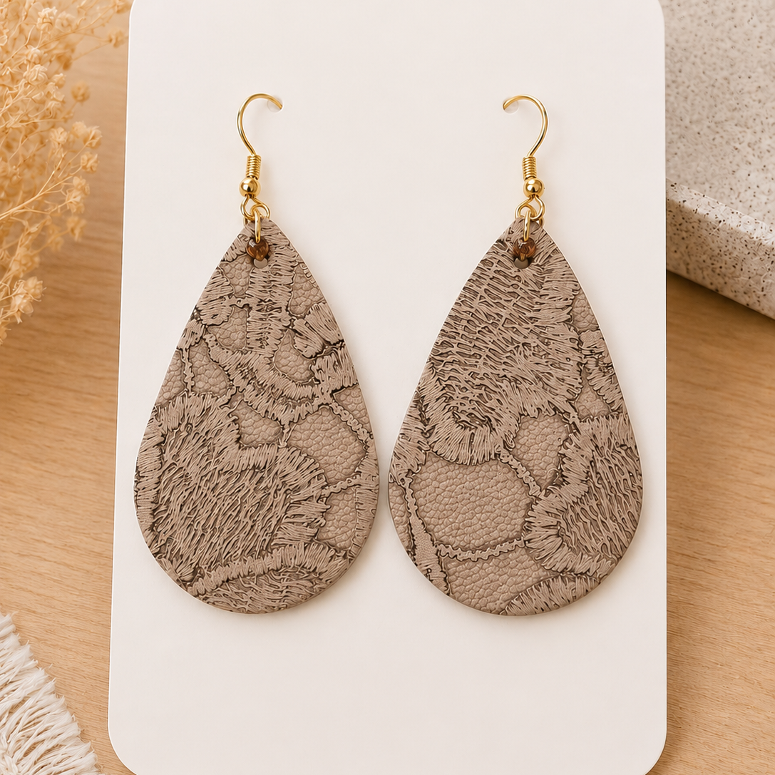 Handmade neutral beige embossed faux leather teardrop earrings with gold hooks displayed on a soft neutral styled card over a light oak surface.