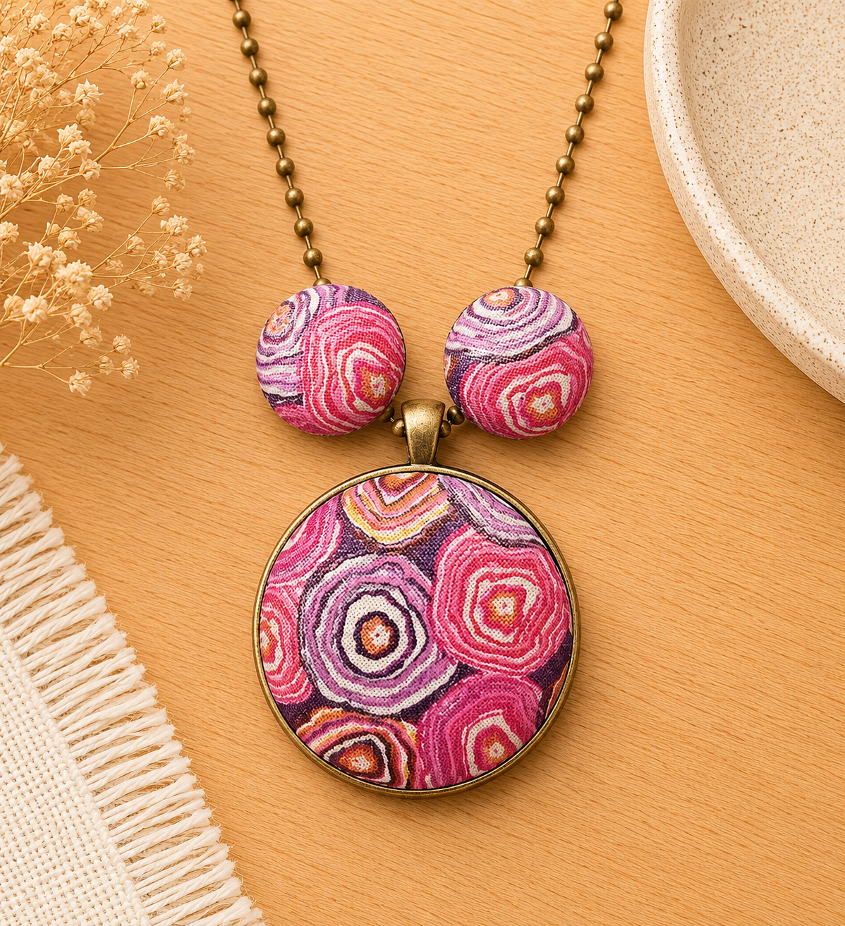 Handmade pink abstract pendant necklace and matching stud earrings with bronze hardware displayed in a soft neutral jewellery setting.