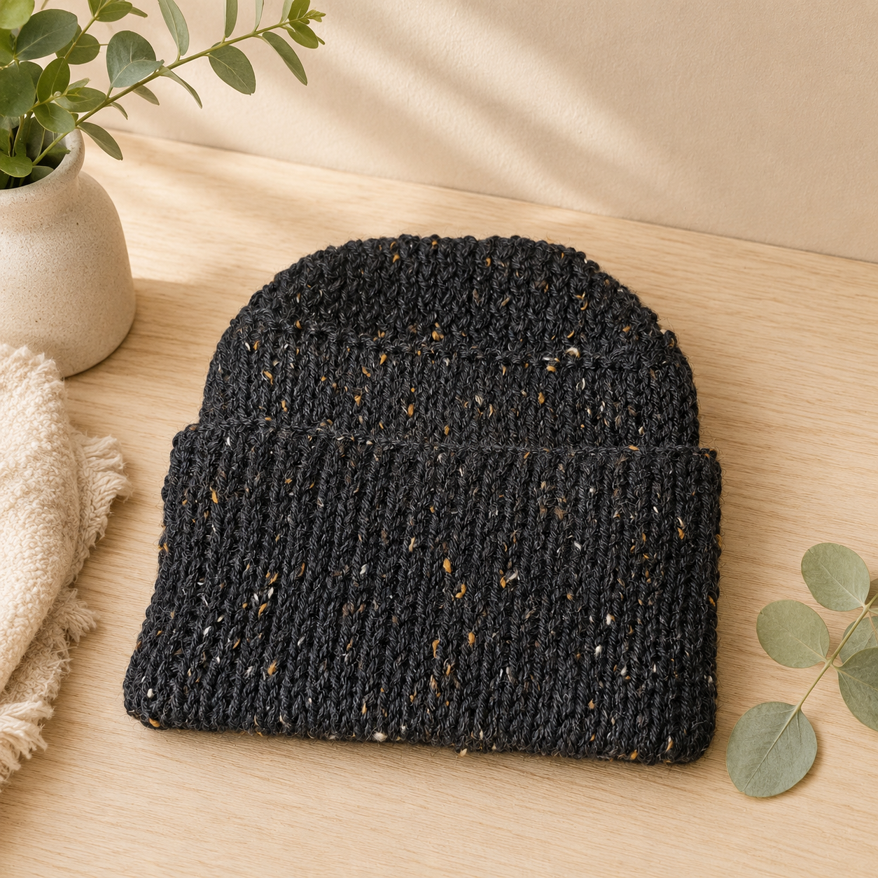 Charcoal fleck wool blend knitted beanie with ribbed cuff styled on a soft neutral light marble background for the Leafy Lovers lifestyle collection.