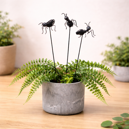 Black wire ant garden stakes placed in a potted fern, decorative outdoor plant accessory