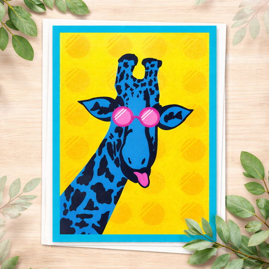 Giraffe blank greeting card with pink sunglasses on a yellow background styled on light wood with greenery