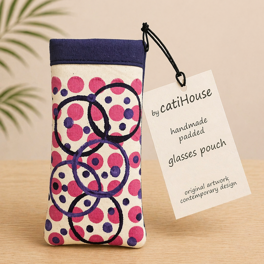Handmade padded glasses pouch with pink and navy circular pattern on light oak surface