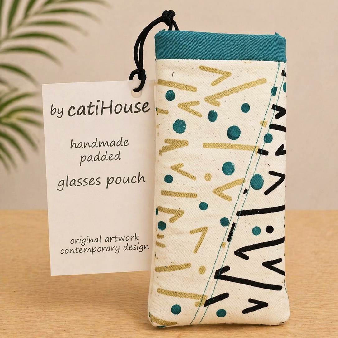 Handmade padded glasses pouch with teal and neutral abstract pattern on light oak surface