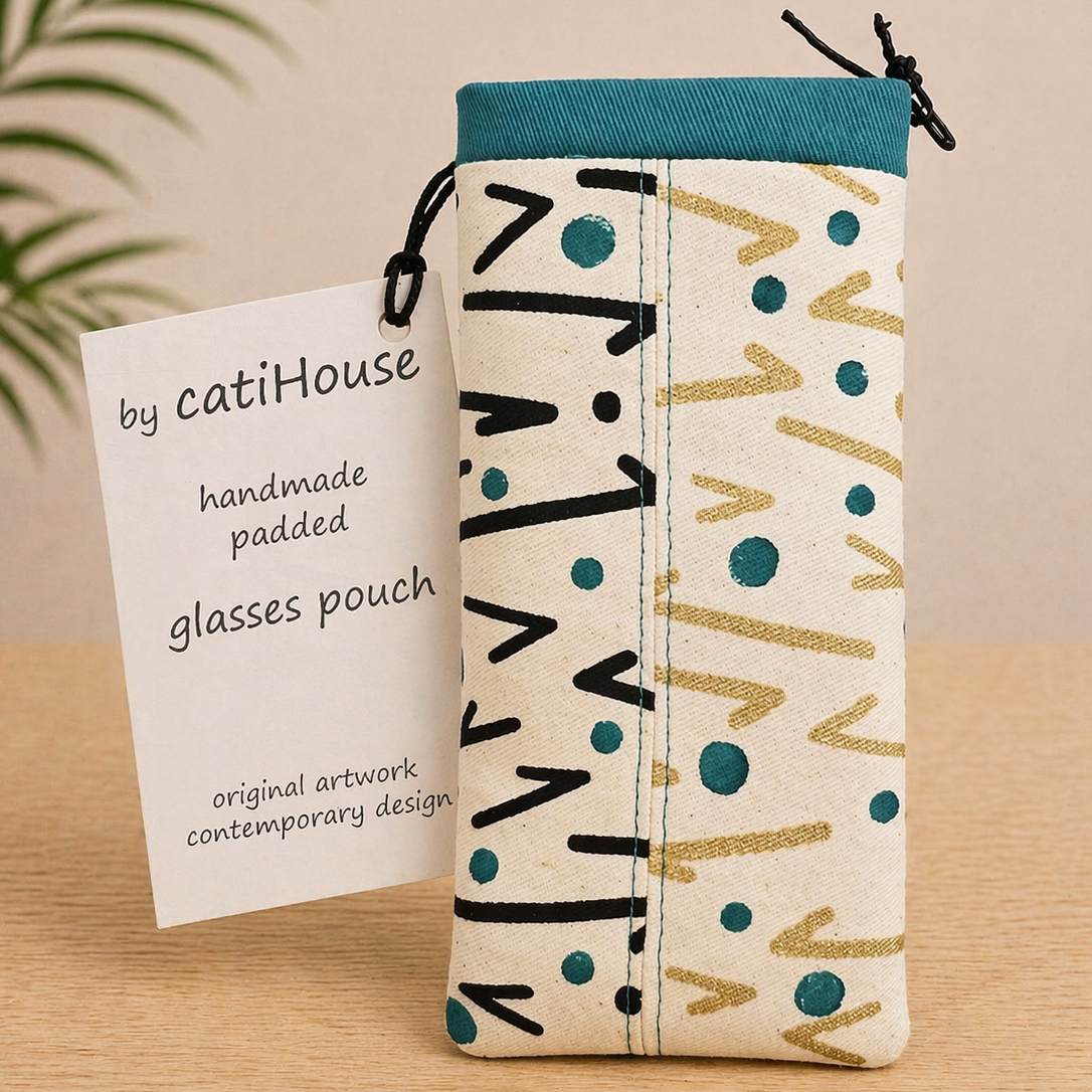 Handmade padded glasses pouch with teal and neutral abstract pattern on light oak surface