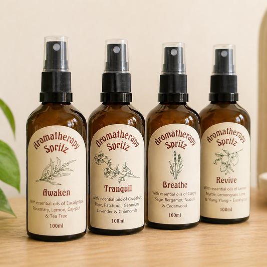Aromatherapy spritz bottles with essential oils on light oak surface in soft neutral setting