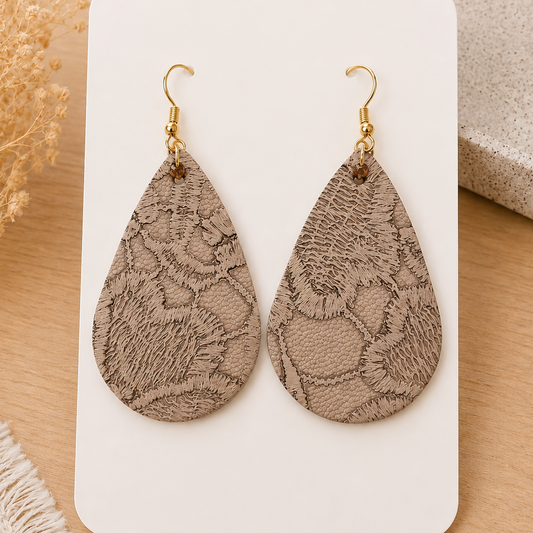 Handmade neutral beige embossed faux leather teardrop earrings with gold hooks displayed on a soft neutral styled card over a light oak surface.