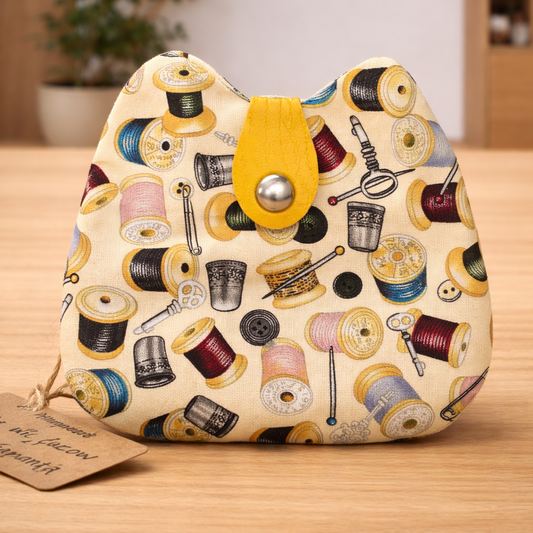 Handmade coin purse with sewing-themed print and snap closure displayed on light oak background