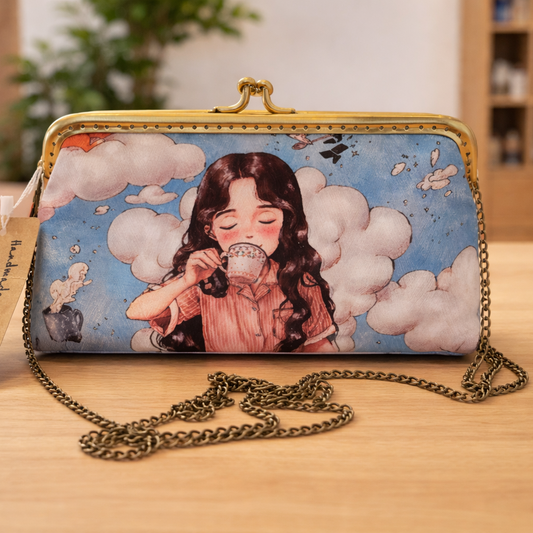 Whimsical illustrated clutch bag with antique frame and chain strap displayed on a light oak surface