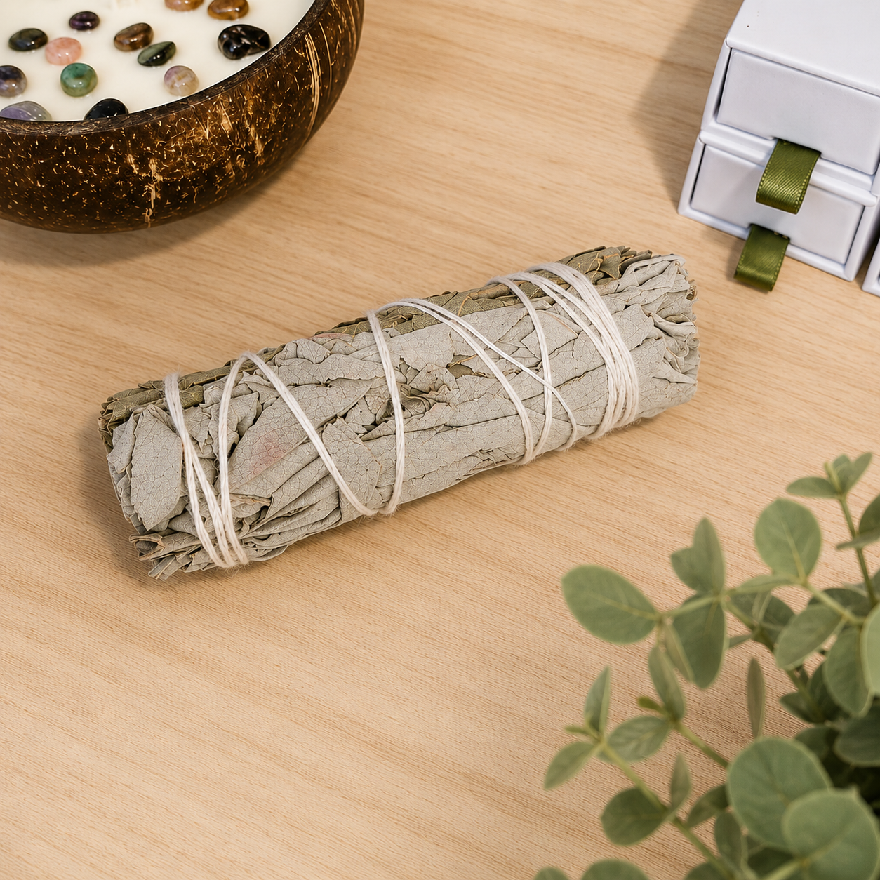 Natural white sage smudge stick displayed on a light oak surface with neutral décor, used for cleansing rituals, meditation and spiritual wellbeing.