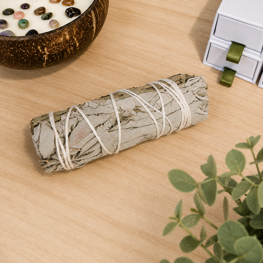 Natural white sage smudge stick displayed on a light oak surface with neutral décor, used for cleansing rituals, meditation and spiritual wellbeing.